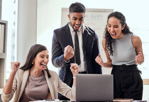 Shot if a group of young businesspeople cheering while using a laptop at work When your hard work pays off passion stock pictures, royalty-free photos & images