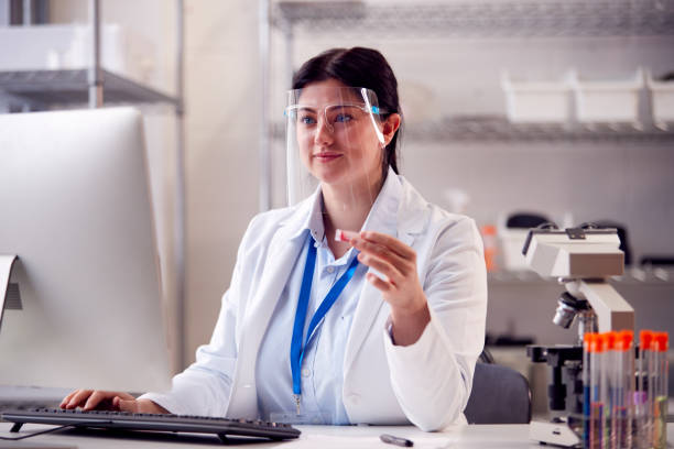 istock Female Lab Worker Wearing White Coat Recording Test Results On Computer 1365603899