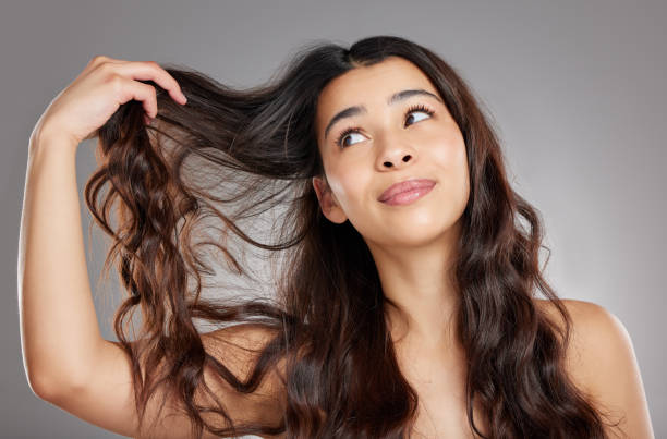 studioaufnahme einer attraktiven jungen frau, die ihr haar vor einem grauen hintergrund hält - frizzy hairstyle human hair women stock-fotos und bilder