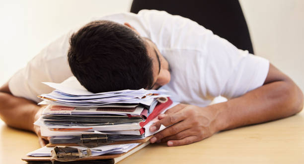 istock Shot of an unrecognisable man asleep on a stack of paperwork while working from home 1365604659
