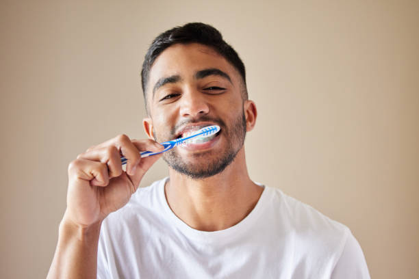 foto de estudio de un apuesto joven cepillándose los dientes contra un fondo de estudio - brushing teeth fotografías e imágenes de stock