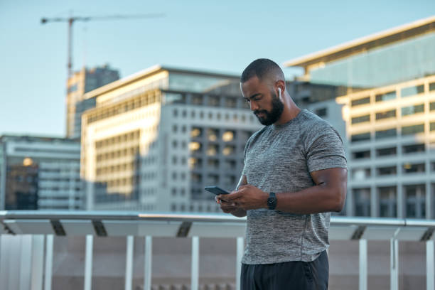 Cropped shot of a handsome young male athlete checking his messages while working out in the city stock photo
