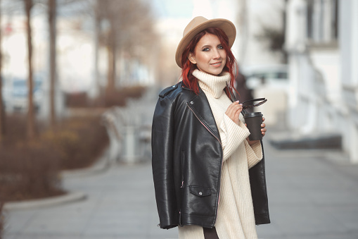 Urban fashion portrait of stylish millennial woman in modern clothes walking on city street. High quality photo