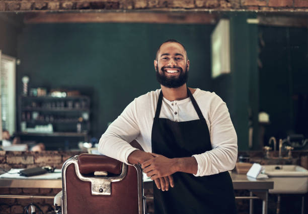 foto seorang tukang cukur muda tampan berdiri sendirian di salonnya - barbershop potret stok, foto, & gambar bebas royalti