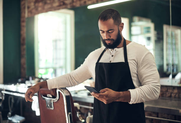 istock Shot of a handsome young barber standing alone in his salon and using his cellphone 1365608024