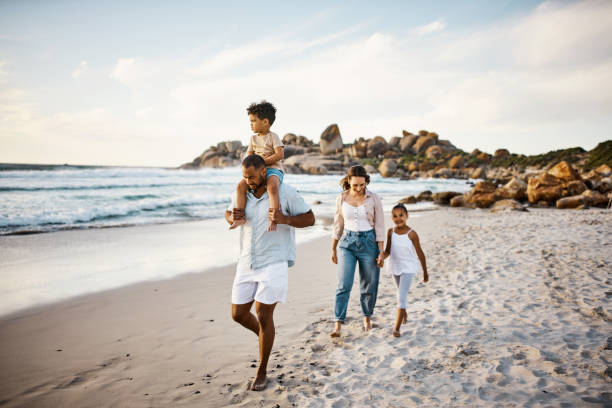 shot of a young couple and their two kids spending the day at the beach - beach two parent family couple family imagens e fotografias de stock