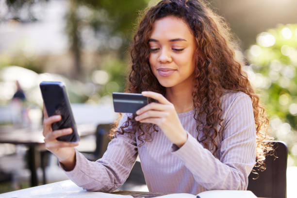 scatto di una giovane donna che usa una carta di credito e un telefono in un bar - credit card shopping retail buying foto e immagini stock
