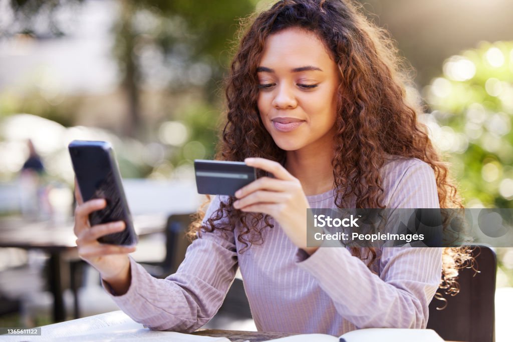 Shot of a young woman using a credit card and phone at a cafe I should probably spoil myself in advance Credit Card Stock Photo