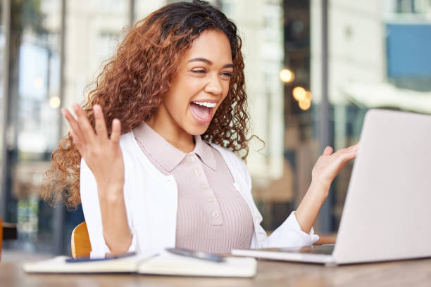 shot of a young businesswoman looking excited while using a laptop at a cafe - excitement business person ecstatic passion imagens e fotografias de stock