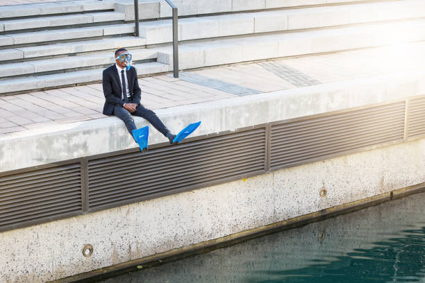 shot of a businessman sitting at the edge of a body of water in scuba diving gear - funny scene imagens e fotografias de stock