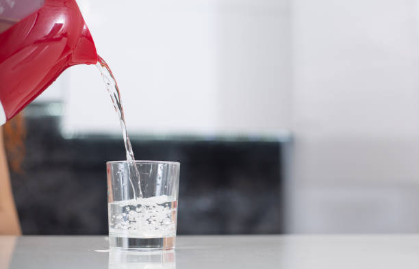istock Woman pouring water from red kettle into a glass on white table 1365611462