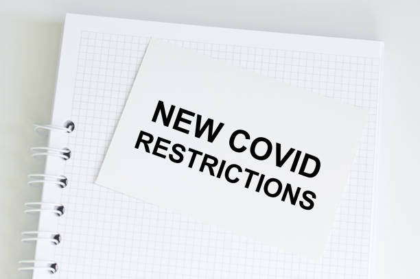 istock text new covid restrictions on a card that sits on a blank notebook on a table, a medical concept 1365614862