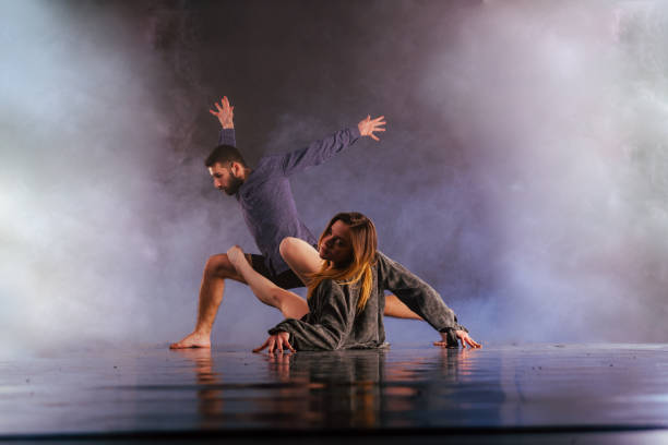 istock Shoeless dance couple performing multiple unique dance moves in front of a black background surrounded by a lot of smoke. 1365615879