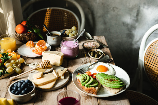 Fresh and healthy breakfast served on table. Avocado toast, fried egg, cheese, honey, smoothie and fresh fruits on wooden breakfast table.