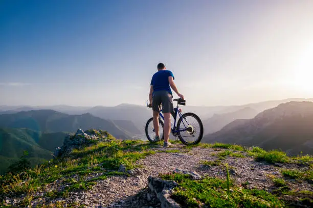 Adventurous Cyclist riding his mountain bike at the edge of a cliff, on rocky terrain while wearing no safety equipment.Amazing top view.