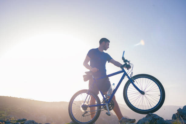 istock Mountain biker holding his bike on a rough cliff terrain on a sunset. 1365616717