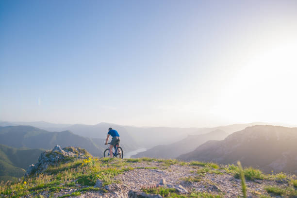 istock Mountain biker holding his bike on a rough cliff terrain on a sunset. 1365616729