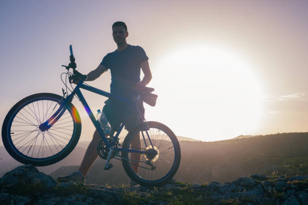 istock Mountain biker holding his bike on a rough cliff terrain on a sunset. 1365616731