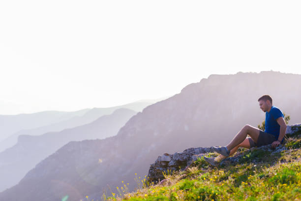 istock Adventurous man sitting on top of a mountain and enjoying the beautiful view, while looking downhill at the blue river and amazing mountain line. 1365616745
