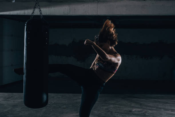 istock Young silhouette female practicing high kick with the boxing bag inside the garage. 1365617008