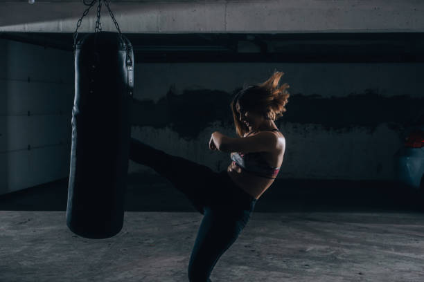 istock Young silhouette female practicing high kick with the boxing bag inside the garage. 1365617017