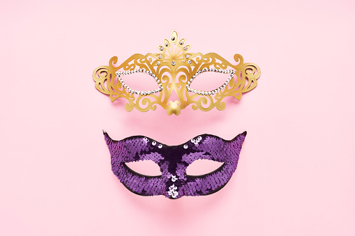 Two colorful carnival masks on a light pink background. Carnival celebration concept. Top view, copy space