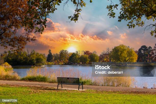 Empty Park Bench Sits By The Water With The Light Of Sunset In The Background Stock Photo - Download Image Now