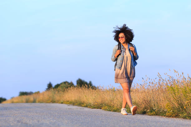 woman in a simple dress walks along a path in a spring field with poppies flowers in her hands. simple real photo of simple life