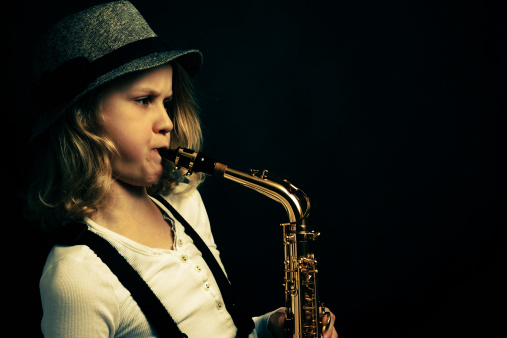 Young girl playing saxophone on dark background. Cross pressed image. Film grain added.