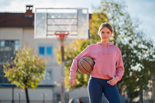 Low angle view of young woman in sportswear holding a ball taking a break while playing basketball as morning workout routine