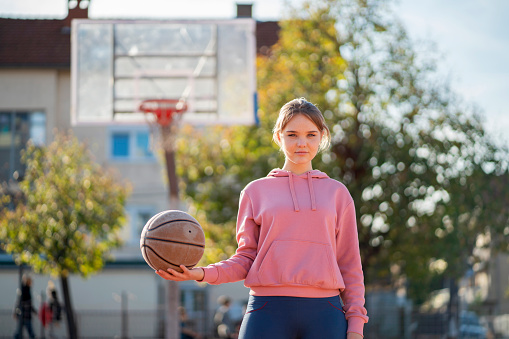 Portrait of Caucasian teenage girl, holding the basketball ball, at the outdoor sports court