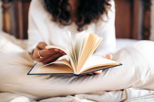 Joven irreconocible pasando las páginas de un libro mientras lee en la cama cubierta con el edredón nórdico photo