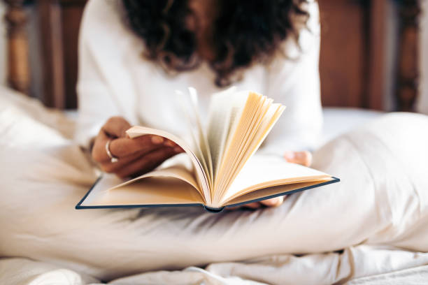 joven irreconocible pasando las páginas de un libro mientras lee en la cama cubierta con el edredón nórdico - leer fotografías e imágenes de stock
