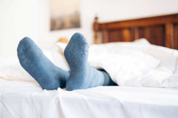 Feet with blue socks sticking out from under the duvet in bed Feet with blue socks sticking out from under the duvet in bed heat home interior comfortable human foot stock pictures, royalty-free photos & images