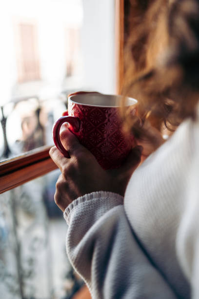 istock Unrecognizable woman drinking coffee by the window (close up) 1365626722