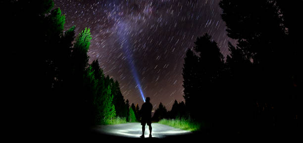 istock Man Standing in Dark Stars with Flashlight Forest Night Sky 1365626953