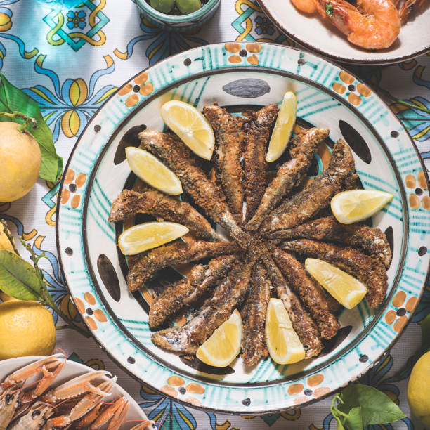 Grilled or fried sardines in the southern Italian style, served on a typical Sicilian dish and tablecloth, with lemon. Seafood dishes, square crop