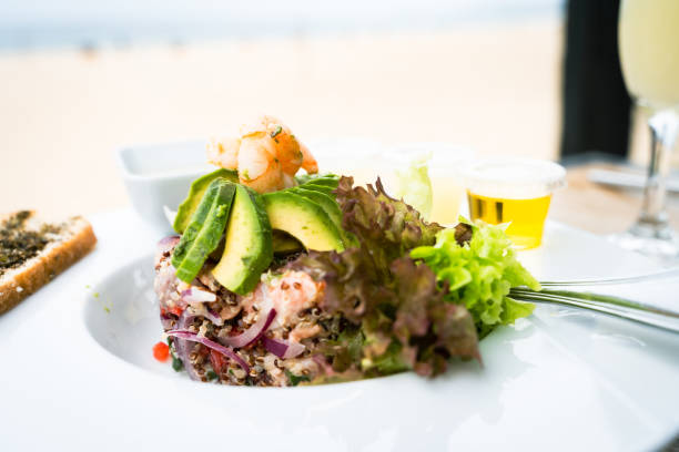 Fresh seafood ceviche plate with quinoa and lettuce on side. Chopped salmon, prawns and avocado slices on top. Gourmet restaurant food concept