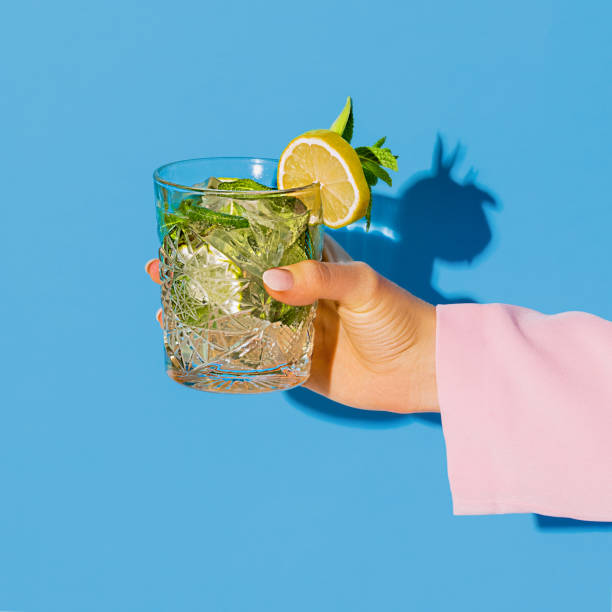 bicchiere femmina che tiene la mano con cocktail mojito con limone isolato su sfondo neon azzurro. concetto di gusto, bevande alcoliche - folding hands foto e immagini stock