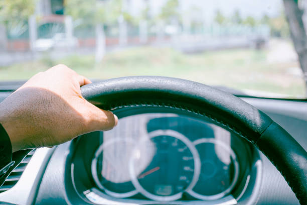 istock Driver's hands on the steering wheel inside of a car, While driving in the sunlight in front of the driver. 1365634188
