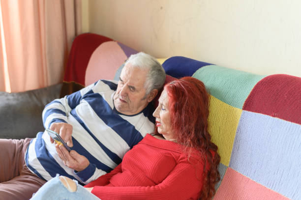 istock Cute elderly couple using cell phone on the sofa at home 1365637814