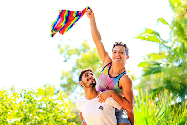 feliz pareja gay pasando tiempo juntos en un día soleado en el parque verde - gay pride flag gay pride gay man homosexual fotografías e imágenes de stock