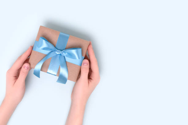 istock Female hands hold wrapped gift box on a blue background. Present tied with a ribbon. 1365638487