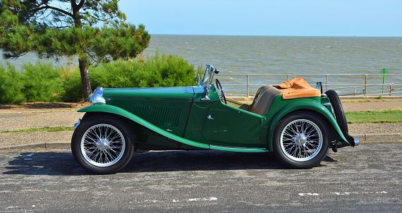 Felixstowe, Suffolk, England - August 21, 2019: Classic Green MG parked on coastal road with the ocean in the background.