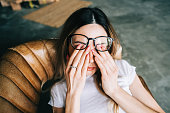 Young woman rubs her eyes after using glasses. Eye pain or fatigue concept.