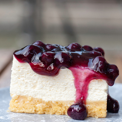 Piece of cheesecake topping with black currant and blueberry sauce serve on white plate.