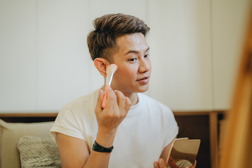 Drag artist - young man drawing new eyebrows in front of the small mirror