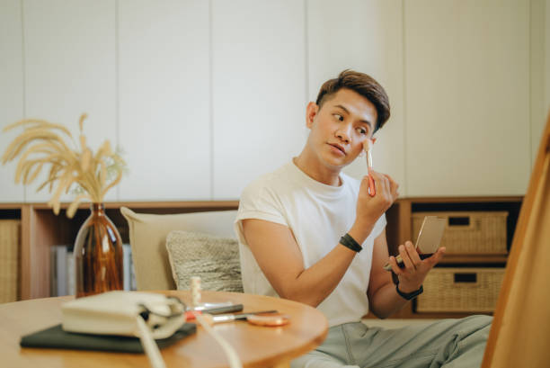 Asian non-binary gender person applying makeup in dressing room. stock photo