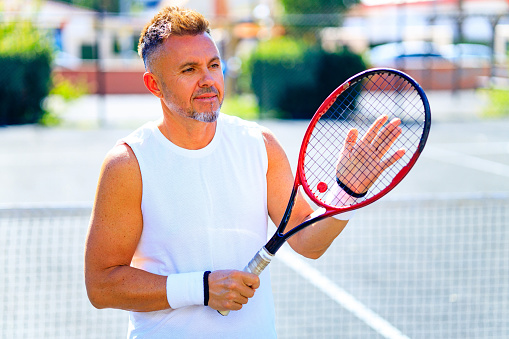 Senior caucasian man playing tennis on court holding tennis racket day light outdoors on fresh air.