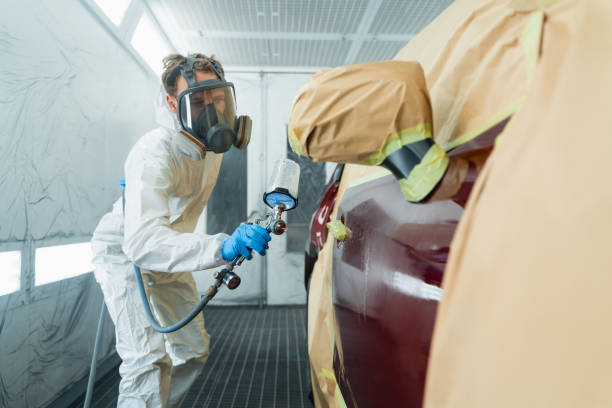 auto pintor em um traje de proteção e máscara pulveriza um mais fino ou outro limpador na porta de um carro usando uma pistola de spray. preparação de elementos da carroceria do veículo para reparo local - car repairing body accident - fotografias e filmes do acervo